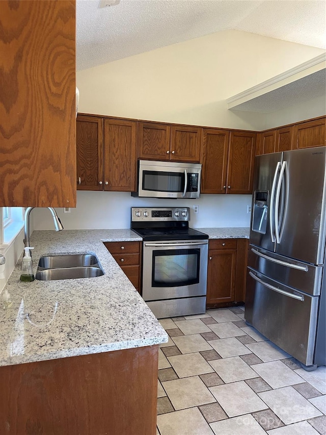 kitchen with light stone countertops, lofted ceiling, stainless steel appliances, a textured ceiling, and a sink