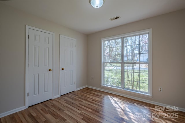 unfurnished bedroom with visible vents, multiple windows, baseboards, and wood finished floors