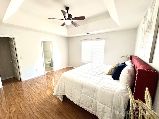 bedroom featuring a raised ceiling, connected bathroom, ceiling fan, and light hardwood / wood-style flooring