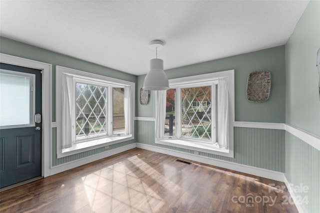 unfurnished dining area featuring a textured ceiling and hardwood / wood-style flooring