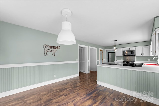 kitchen featuring dark wood-type flooring, kitchen peninsula, hanging light fixtures, white cabinetry, and appliances with stainless steel finishes