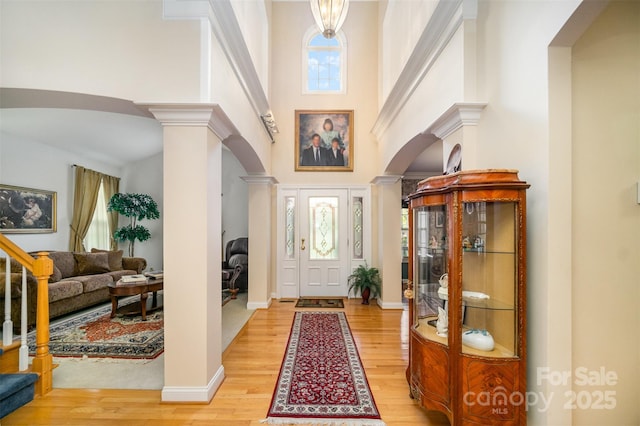 foyer entrance with light hardwood / wood-style flooring, a towering ceiling, and ornate columns