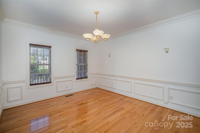 spare room with wood-type flooring, ornamental molding, and a chandelier