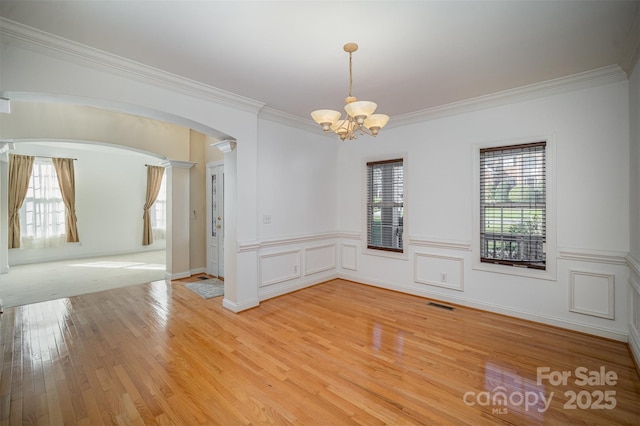 spare room featuring a wealth of natural light, ornamental molding, light hardwood / wood-style floors, and an inviting chandelier