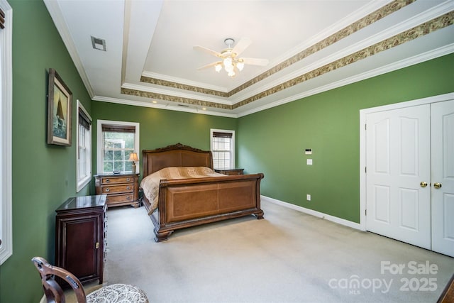 carpeted bedroom with ceiling fan, ornamental molding, a closet, and a tray ceiling