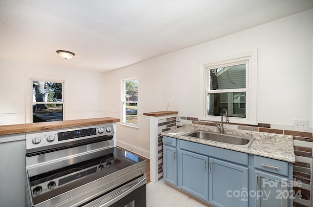 kitchen featuring stainless steel stove, light stone countertops, sink, and blue cabinets