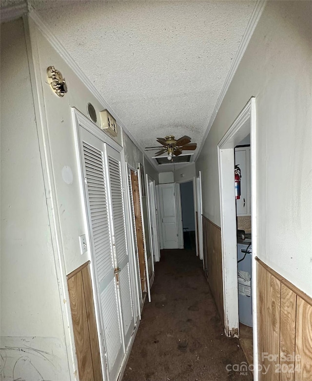 hall featuring wood walls, crown molding, and a textured ceiling