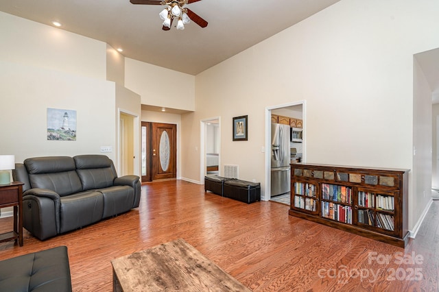 living room featuring ceiling fan, wood-type flooring, and a towering ceiling