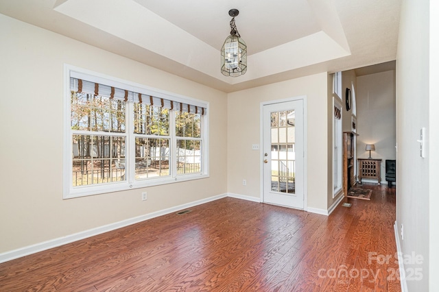 spare room with a tray ceiling, dark hardwood / wood-style flooring, and a notable chandelier