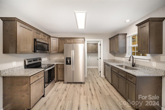 kitchen with light stone countertops, sink, dark brown cabinets, appliances with stainless steel finishes, and light wood-type flooring