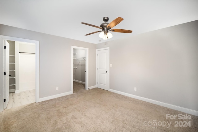 unfurnished bedroom with ceiling fan, light colored carpet, a walk in closet, and a closet