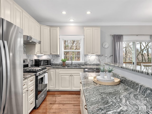 kitchen with white cabinetry, sink, dark stone countertops, light hardwood / wood-style floors, and appliances with stainless steel finishes