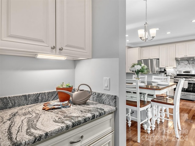 kitchen featuring stone counters, an inviting chandelier, white cabinets, light wood-type flooring, and appliances with stainless steel finishes