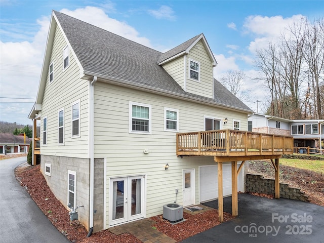 rear view of property with a shingled roof, central AC, aphalt driveway, a garage, and a wooden deck