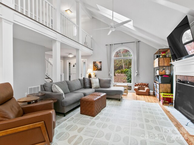 living room featuring a fireplace, light wood-type flooring, beam ceiling, high vaulted ceiling, and ceiling fan