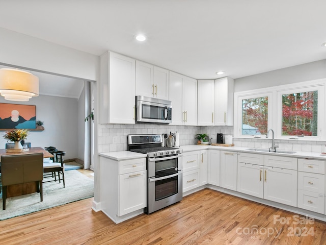 kitchen with stainless steel appliances, light hardwood / wood-style floors, white cabinetry, and sink