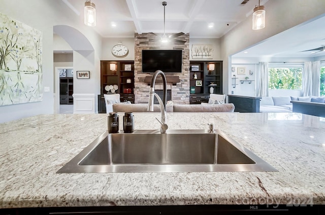 kitchen featuring sink, hanging light fixtures, coffered ceiling, built in shelves, and light stone counters