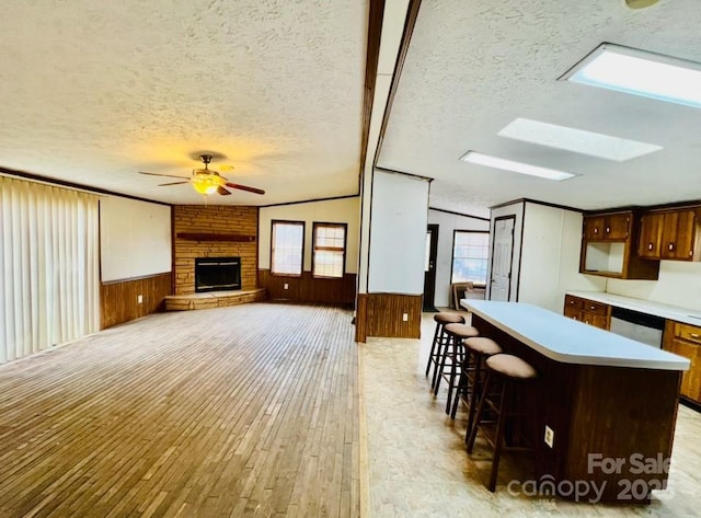 kitchen featuring a kitchen breakfast bar, vaulted ceiling, ceiling fan, wooden walls, and a fireplace