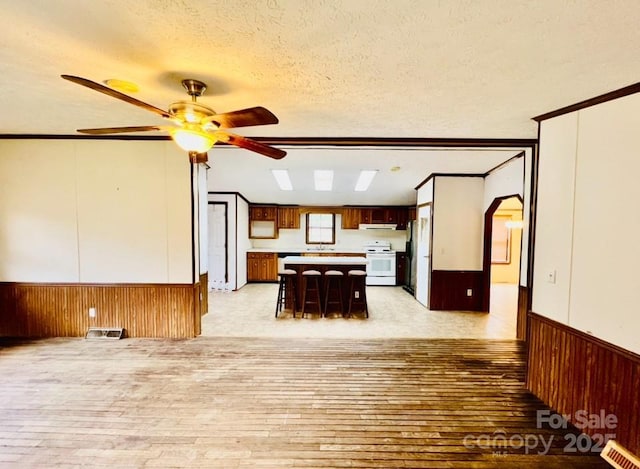 unfurnished dining area featuring ceiling fan, light hardwood / wood-style flooring, a textured ceiling, and ornamental molding