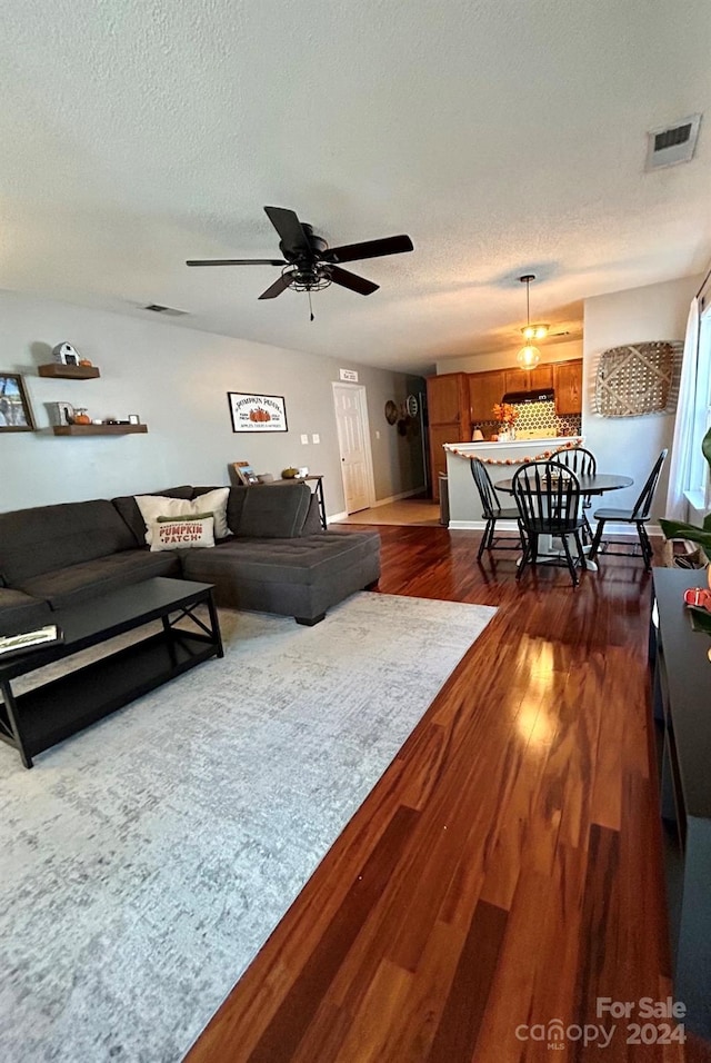 living room with dark wood-type flooring, a textured ceiling, and ceiling fan