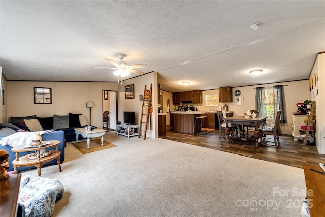 living room featuring dark colored carpet, a textured ceiling, ceiling fan, and ornamental molding