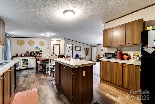 kitchen with dark hardwood / wood-style floors, a textured ceiling, lofted ceiling, a kitchen island, and black appliances