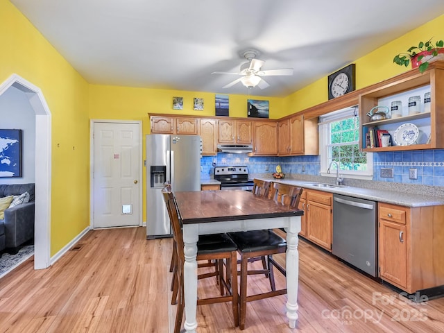 kitchen featuring light wood-type flooring, backsplash, stainless steel appliances, and ceiling fan