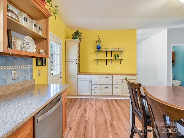 kitchen with stainless steel dishwasher, decorative backsplash, light wood-type flooring, and light stone countertops