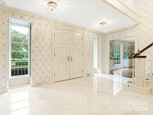 foyer entrance featuring crown molding, a wealth of natural light, and an inviting chandelier