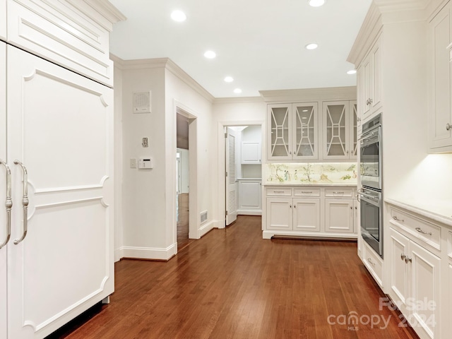 kitchen with backsplash, dark wood-type flooring, white cabinets, ornamental molding, and double oven