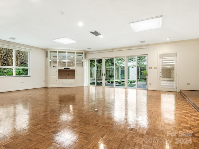 unfurnished living room with parquet flooring, a healthy amount of sunlight, and ornamental molding