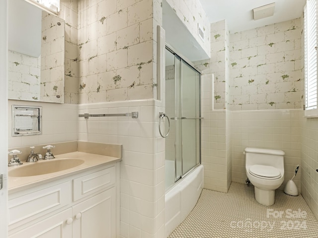 full bathroom with tile patterned flooring, enclosed tub / shower combo, toilet, vanity, and tile walls