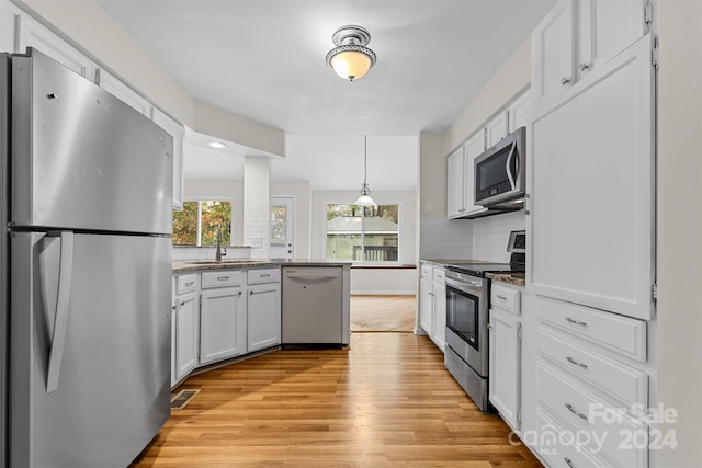 kitchen featuring white cabinetry, appliances with stainless steel finishes, backsplash, hanging light fixtures, and light wood-type flooring