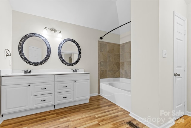 bathroom with hardwood / wood-style floors, vanity, and tiled shower / bath