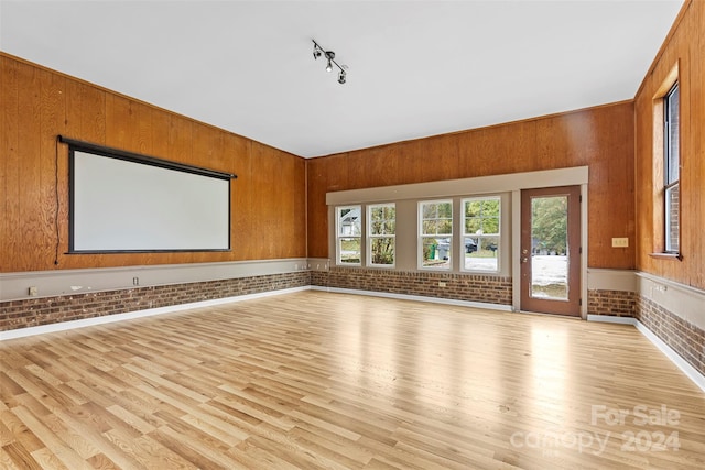 empty room featuring plenty of natural light, wooden walls, brick wall, and light wood-type flooring