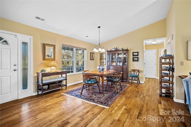 dining space with wood-type flooring, lofted ceiling, and a notable chandelier