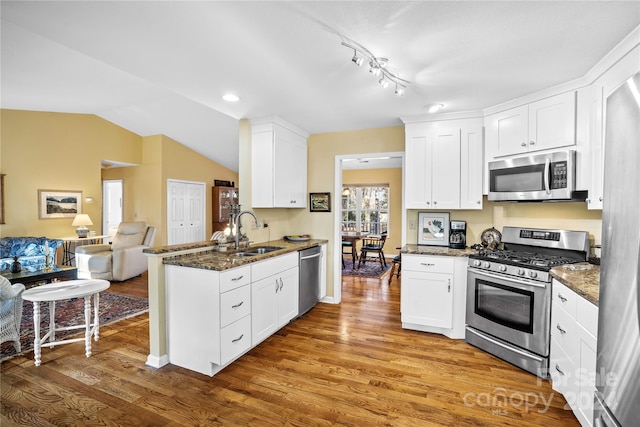 kitchen with hardwood / wood-style flooring, white cabinetry, sink, appliances with stainless steel finishes, and lofted ceiling