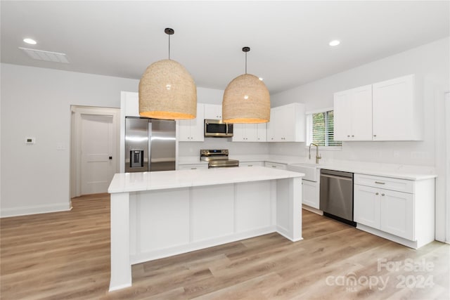 kitchen featuring stainless steel appliances, pendant lighting, white cabinetry, light hardwood / wood-style flooring, and a kitchen island