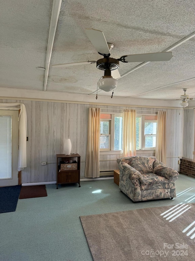 living room with wood walls, a textured ceiling, carpet floors, and ceiling fan