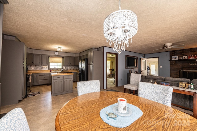 dining space featuring a textured ceiling, a brick fireplace, and ceiling fan with notable chandelier