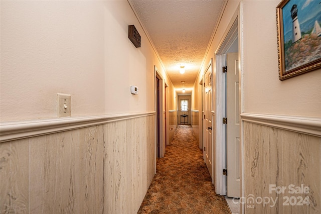 corridor featuring wooden walls, a textured ceiling, and dark carpet