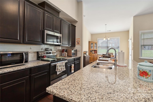 kitchen with appliances with stainless steel finishes, hanging light fixtures, sink, and light stone countertops