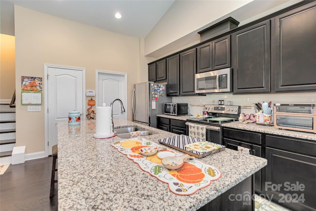 kitchen featuring light stone counters, stainless steel appliances, dark hardwood / wood-style flooring, sink, and a kitchen island with sink