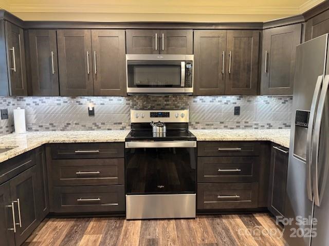 kitchen with appliances with stainless steel finishes, dark hardwood / wood-style flooring, dark brown cabinets, and decorative backsplash