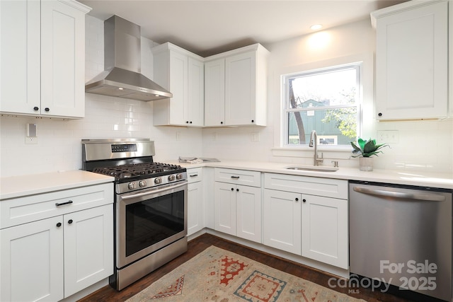 kitchen with light countertops, wall chimney range hood, a sink, and appliances with stainless steel finishes