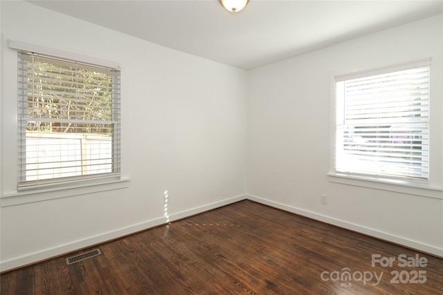 empty room featuring baseboards, visible vents, dark wood finished floors, and a wealth of natural light