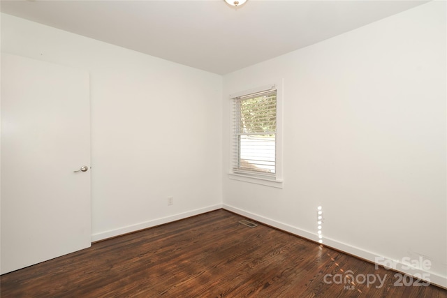 empty room with dark wood finished floors, visible vents, and baseboards