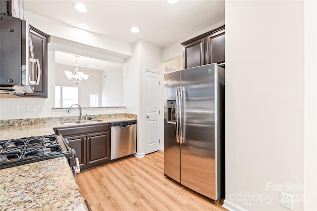 kitchen featuring light wood-type flooring, appliances with stainless steel finishes, dark brown cabinets, a notable chandelier, and sink