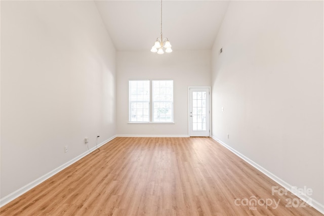 spare room with light hardwood / wood-style floors, an inviting chandelier, and high vaulted ceiling