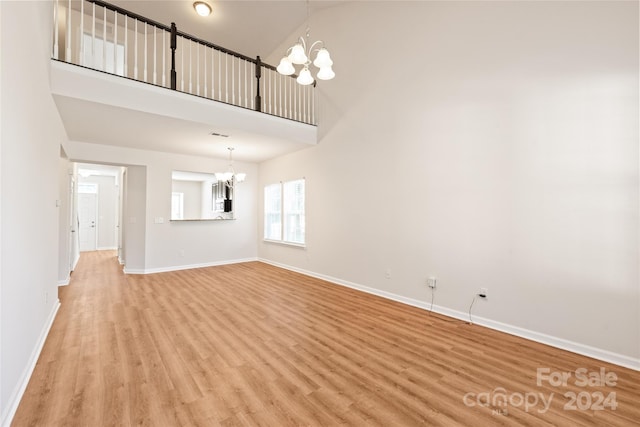 unfurnished living room with high vaulted ceiling, an inviting chandelier, and light hardwood / wood-style floors